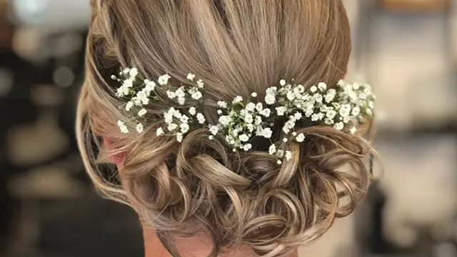 Smukt frisurer med bløde krøller og små hvide blomster i håret, perfekt til en festlig lejlighed.
