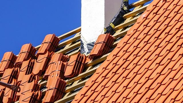 Tag med røde teglsten og en hvid skorsten under en klar blå himmel.