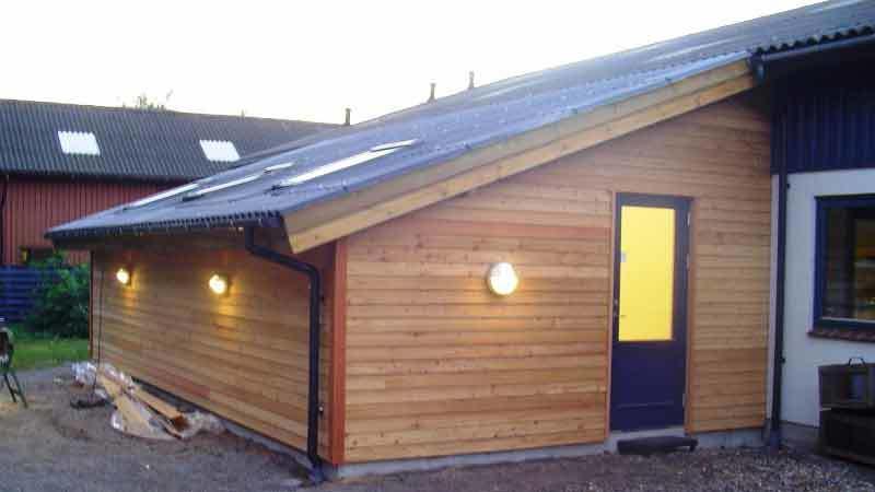 Et moderne hus med træbeklædning, skråtag og gule vinduer, belyst af udendørs lamper.