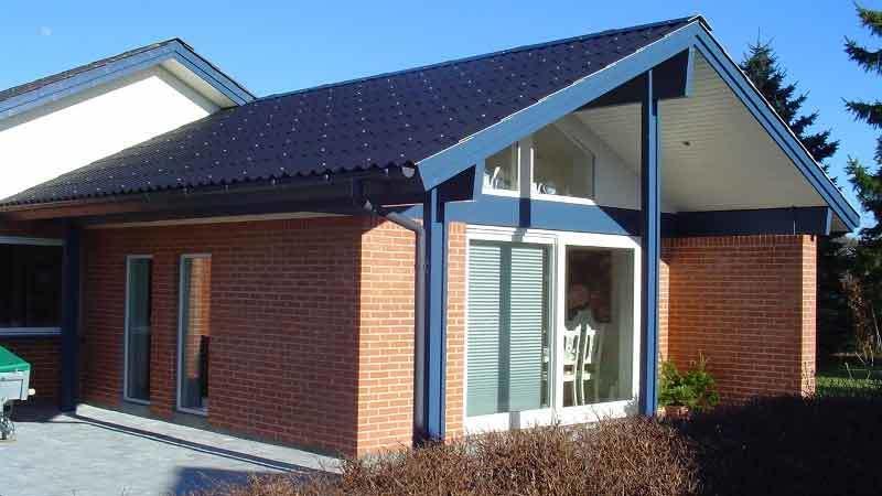 Moderne murstenshus med skråtag og store vinduer, beliggende i en solrig have.
