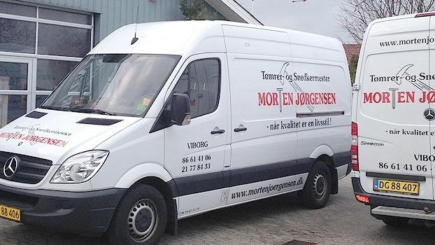 To varevogne med firmalogoet "Morten Jørgensen" parkeret foran en bygning.