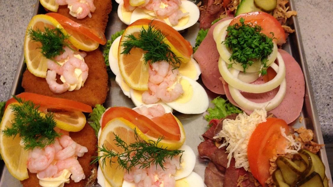 Lækre smørrebrød med rejer, æg, citron, løg og forskellige pålæg på en bageplade.