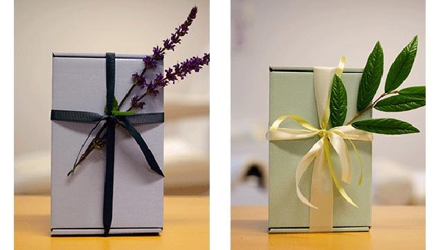 Gaveæsker med bånd og blomsterdekorationer, en med lavendel og en med grønne blade.