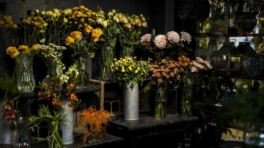 En blomsterbutik med farverige buketter i vaser, herunder roser, dahliaer og chrysantemum.