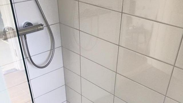 Brusekabine med glasvæg og fliser i hvidt, der viser en ren og moderne badeværelsesindretning.