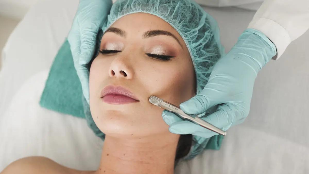 Kvinde får ansigtsbehandling med microneedling, iført hårnet og beskyttelseshandsker.