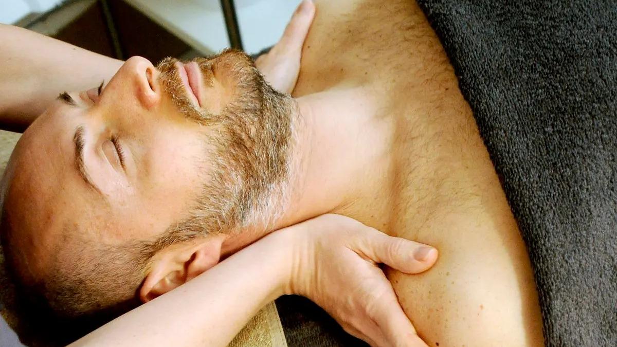 Mand får massage på en briks, mens en behandler arbejder på hans nakke og skuldre.