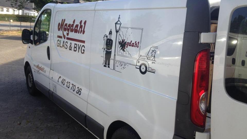 En hvid varevogn med teksten "Magdal" og en tegning af en lampe og en trailer.