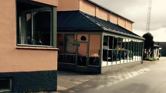 En bygning med store vinduer og en tagterrasse, beliggende på en gade med grå asfalt.