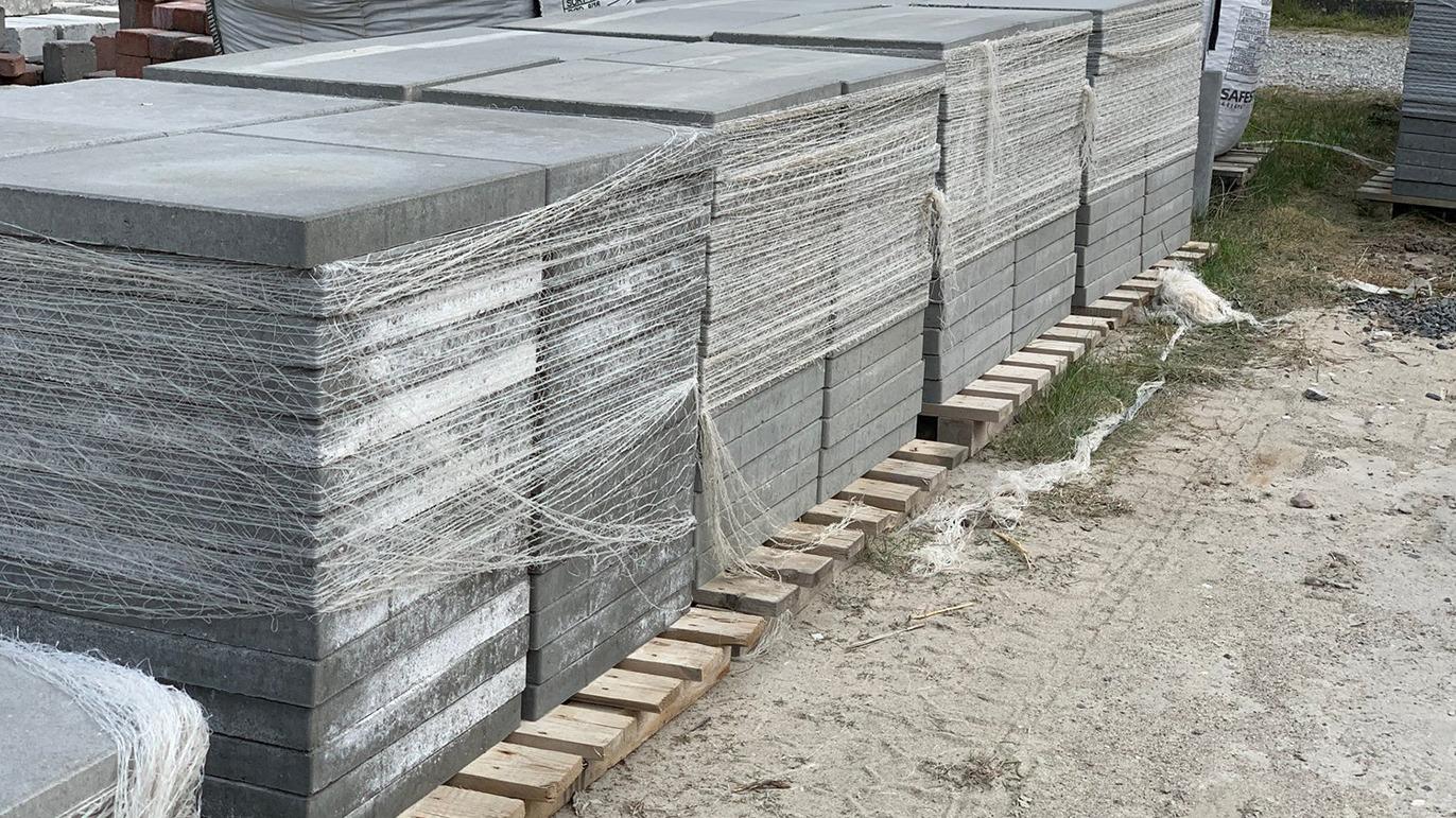 Stabel af grå betonsten pakket ind i plastfolie og snore på en byggeplads.