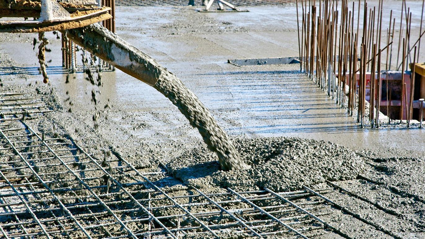 Beton hældes fra en slange på en byggeplads, hvor armeringsjern er synligt under den friske beton.