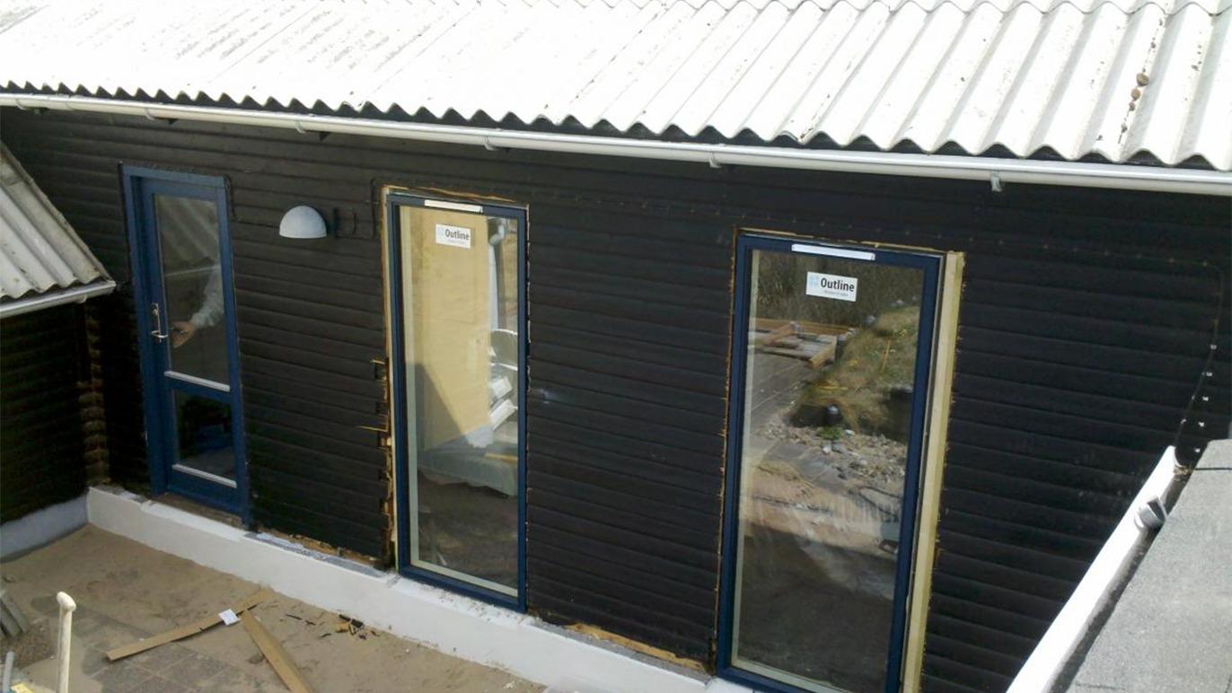 Sort hus med to døre og et vindue, beliggende under et tag med metalplader.