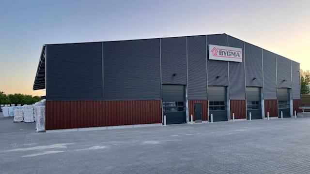 Lagerbygning med grå facade og tre porte, beliggende i et industriområde ved solnedgang.