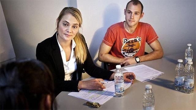 To personer i en samtale ved et bord, med vandflasker og papirer foran dem.