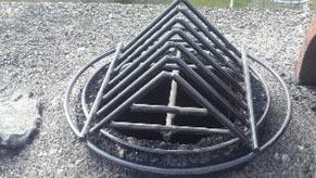 En metalramme i pyramideform placeret over en åbning i en grusbelagt overflade.