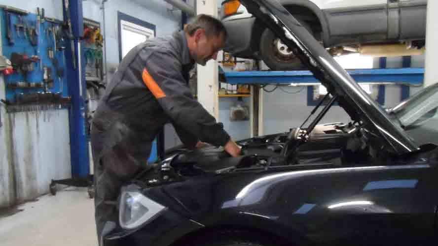 Mekaniker arbejder på motoren i en bil i et værksted med værktøj i baggrunden.