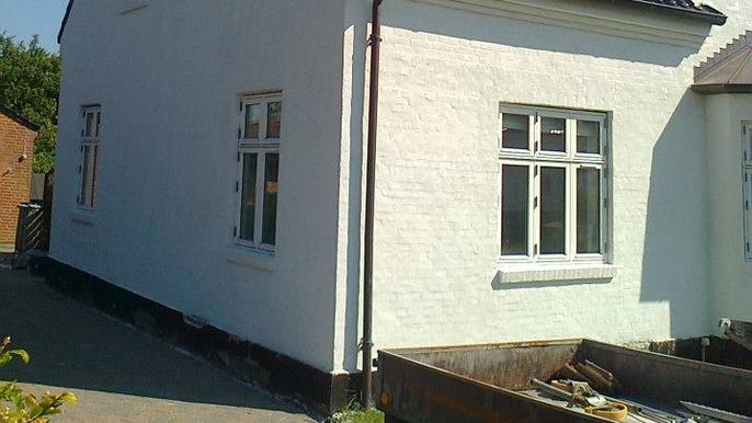 Hvidt hus med vinduer set fra siden, omgivet af grus og en byggeplads.