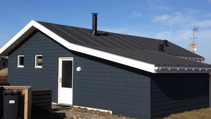 Et moderne hus med sort tag og blå vægge, beliggende i et åbent område med klar himmel.