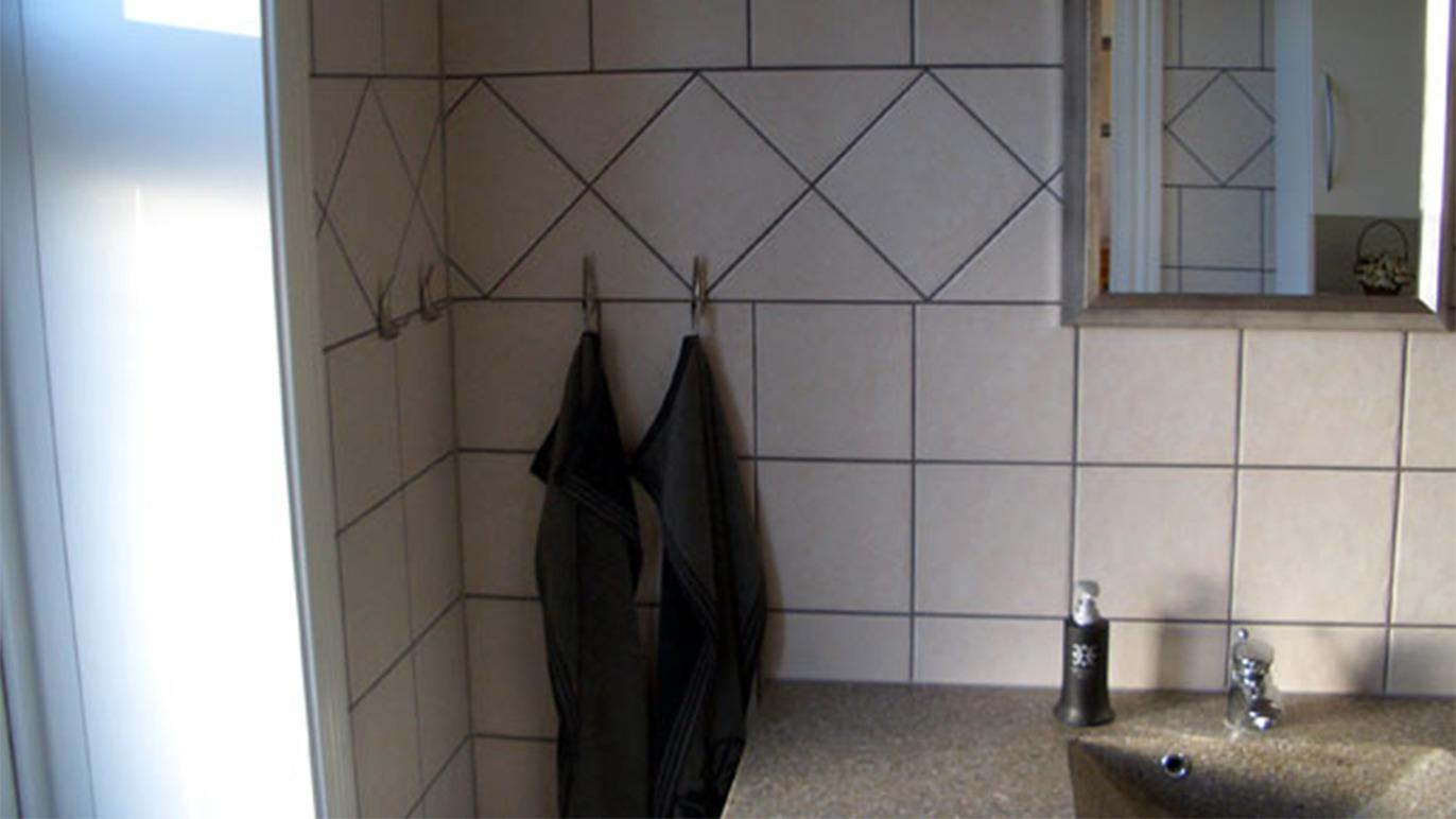 Badeværelse med fliser, håndklæder hængende på kroge og en vask med vandhane.