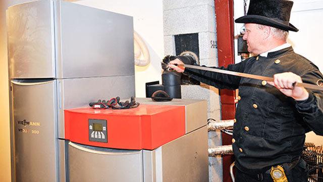 En mand i sort uniform og hat justerer en rød kedel ved siden af en sølvfarvet køleskab.