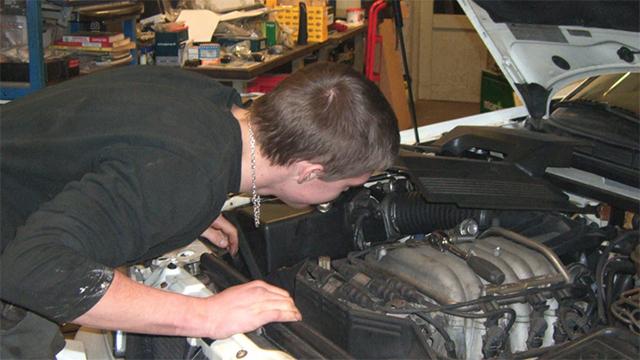 En ung mand kigger ind i motoren på en bil i et værksted.