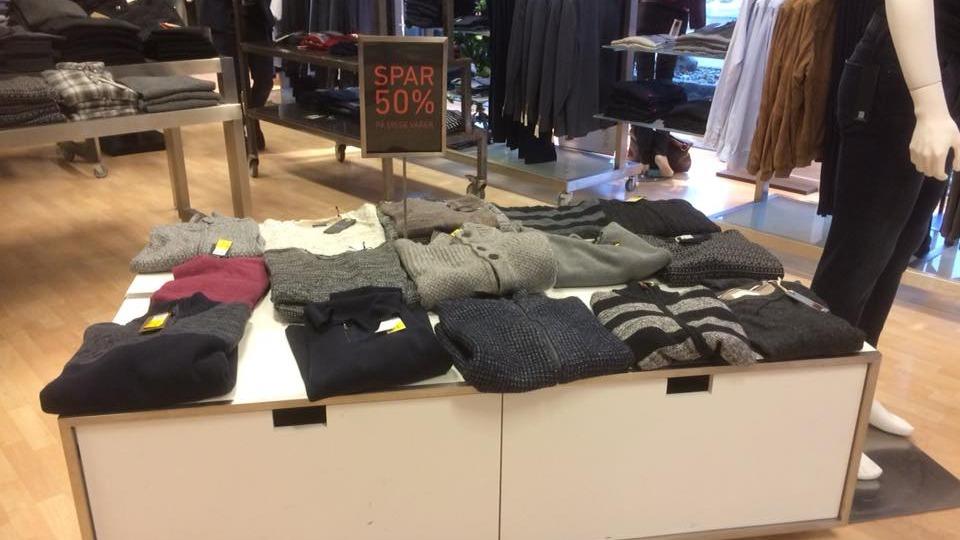 Bord med forskellige trøjer og bluser til salg, med et skilt der viser 50% rabat.