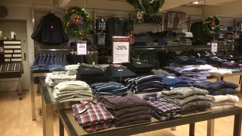 Tøjbutik med borde fyldt med skjorter, bukser og rabatskilt på -20% i en lys og indbydende atmosfære.