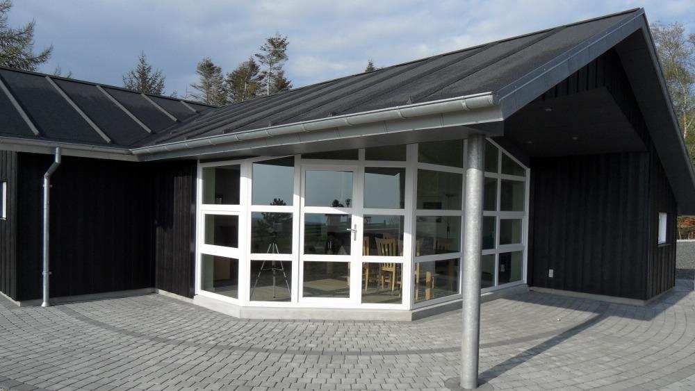 Moderne sort hus med store vinduer og tag i metal, beliggende på en stenbelagt gårdsplads.