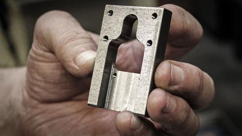 Hånd, der holder en metalblok med en udskæring, der viser detaljer i bearbejdningen.