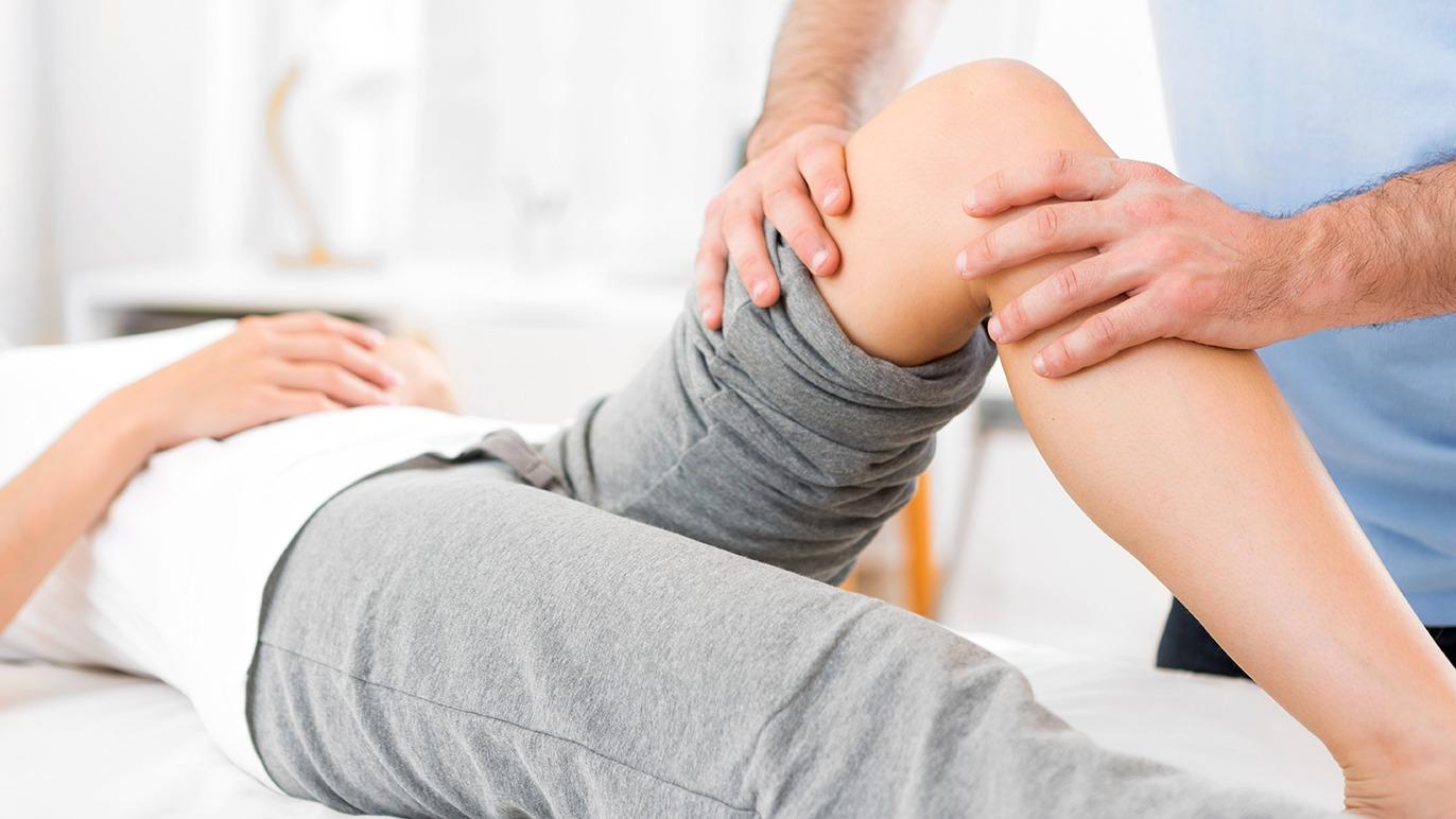 Fysioterapeut udfører knæbehandling på en patient liggende på en behandlingsbænk.