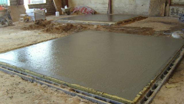 Nyudlagt betonplade på byggeplads med sand og værktøj i baggrunden.