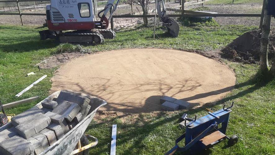 En rund sandplade på en byggeplads med værktøj og en gravemaskine i baggrunden.