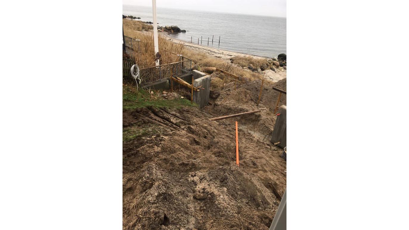 Billede af en kystlinje med mudret jord, byggeri og en vandkant ved havet.