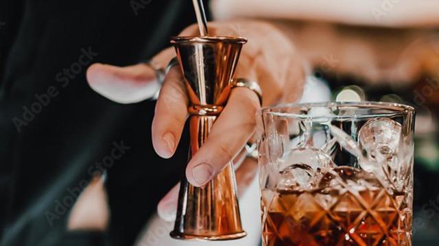 En bartender hælder en drink fra en målekop til et glas med isterninger.