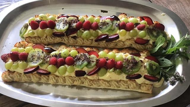 Lækker dessert med to lag kage toppet med flødeskum, frugt og friske urter på en sølvfad.