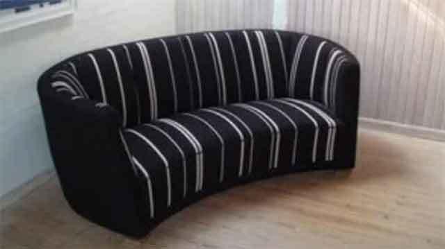 En sort sofa med striber, der står på et lyst trægulv i et rum med hvide vægge.