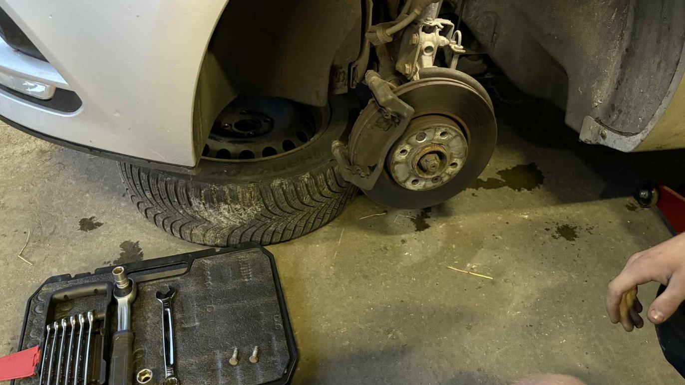 Billede af en bil med et afmonteret hjul, værktøjssæt og en dækkasse på gulvet i en garage.