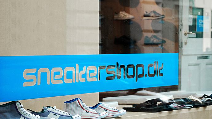 Vinduet til en sneakershop med forskellige sneakers og logoet "sneakershop.dk" i blå farve.