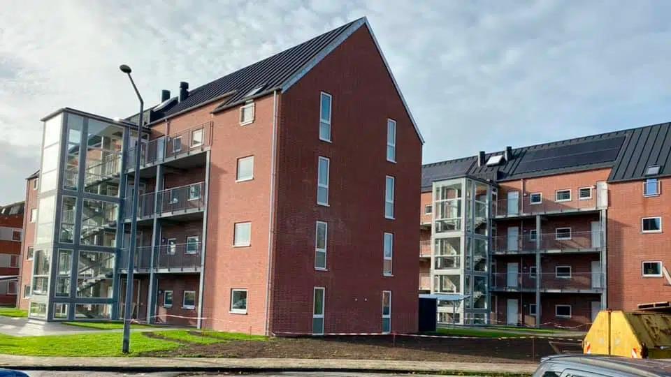 Moderne murstensbygninger med glasbalkoner og skråtag i et boligområde.