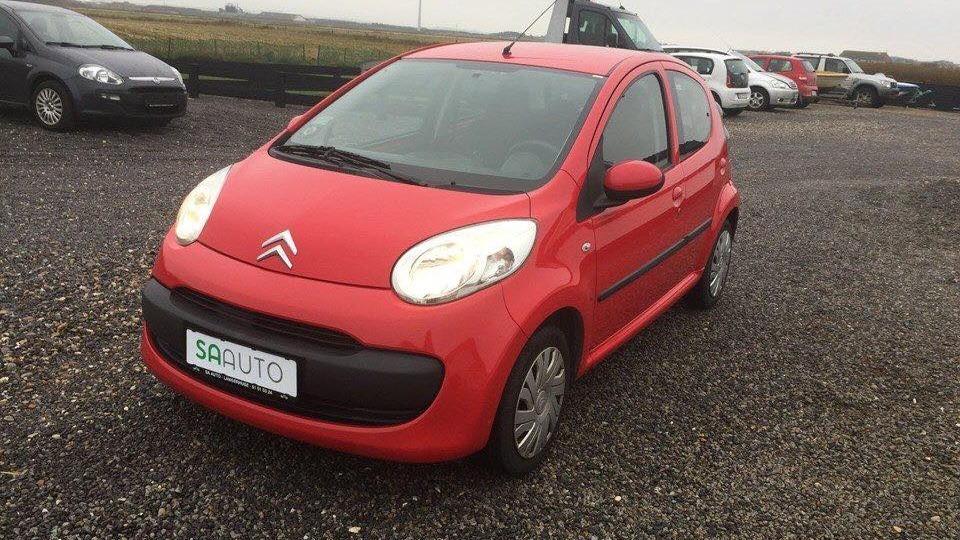 Rød Citroën bil parkeret på en grusplads med andre biler i baggrunden.