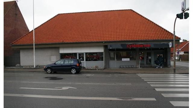 En bygning med rød tagsten og en butik i stueetagen, beliggende ved en vej med fodgængerfelt.