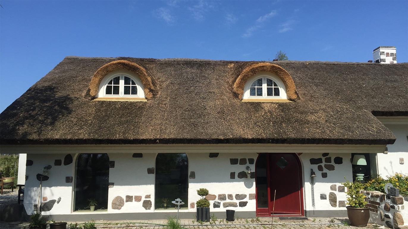 Et charmerende hus med stråtag, rundede vinduer og stenfacade under en klar blå himmel.