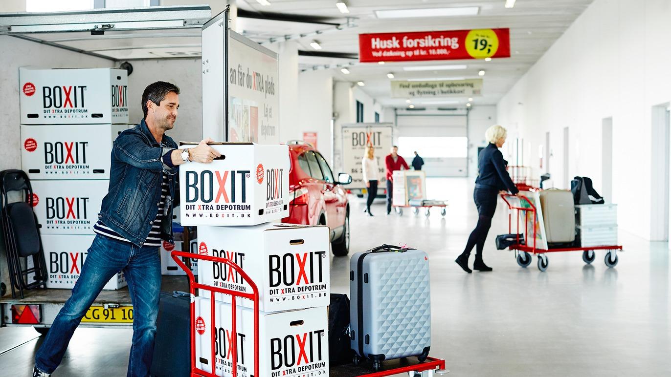 En mand trækker kasser fra en lastbil i en lufthavn, mens en kvinde skubber en bagagevogn.