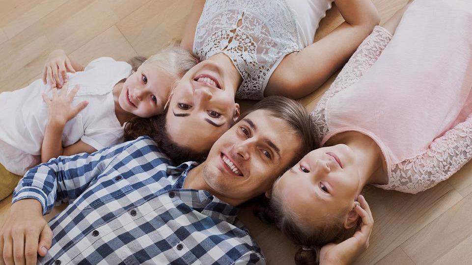 En glad familie ligger på gulvet med smilende ansigtter og ser op mod kameraet.
