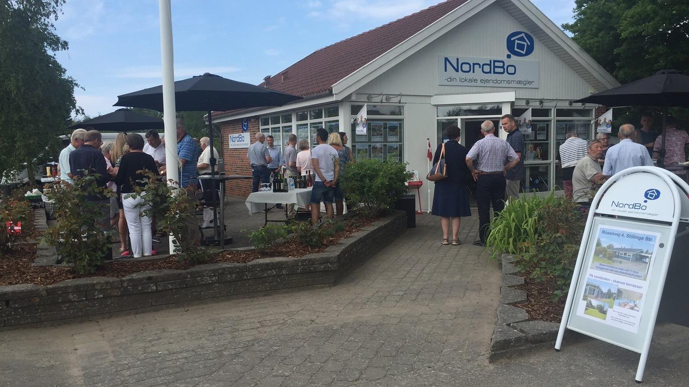 Mennesker samles udenfor NordeBo bygningen, der har parasoller og en informationsskilt.