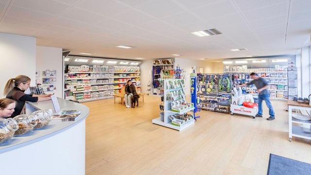 En moderne butik med hylder fyldt med varer, kunder der handler, og en medarbejder ved kassen.