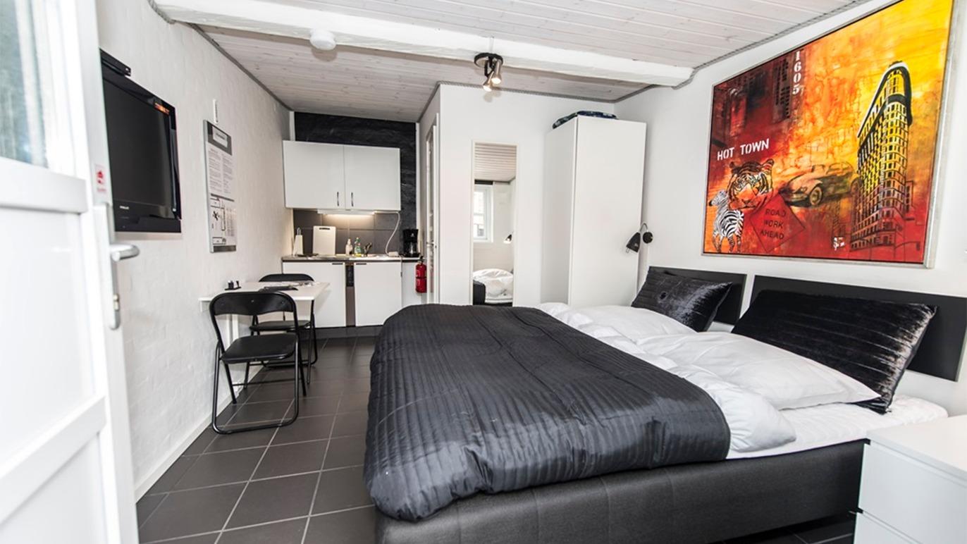 Moderne hotelværelse med dobbeltseng, køkkenkrog og farverigt maleri på væggen.