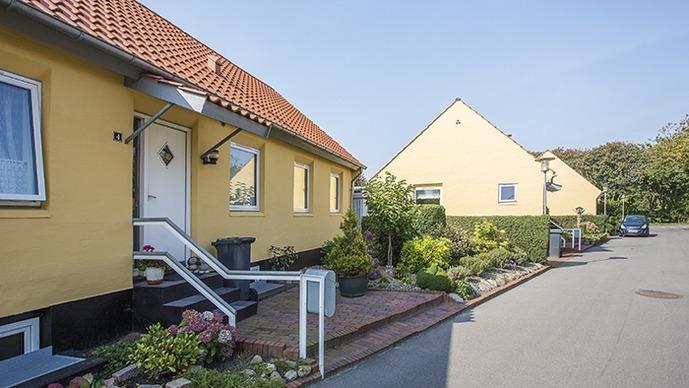 En hyggelig gade med gule huse, blomsterbede og en indgangstrappe til et hus.