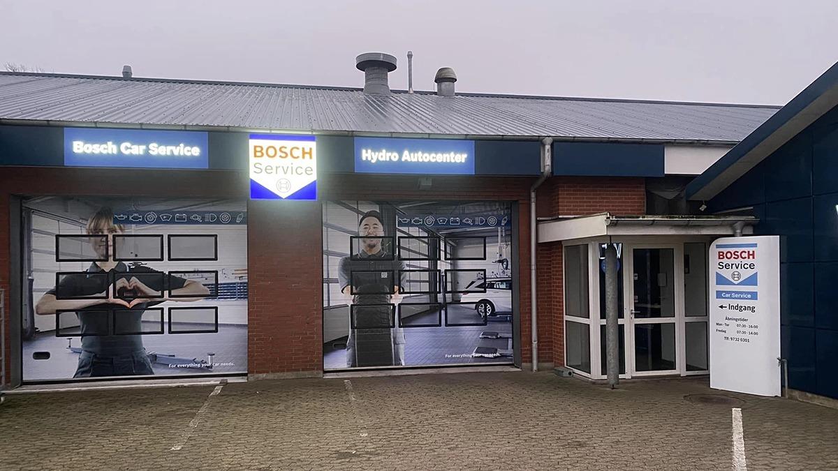 Bosch bilservice med store skilt og indgang til værkstedet, der viser biler og mekanikere i arbejde.