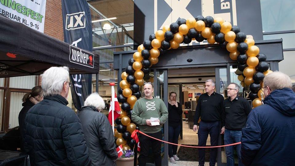 Åbning af en butik med en ballonbue i sort og guld, hvor folk samles foran indgangen.